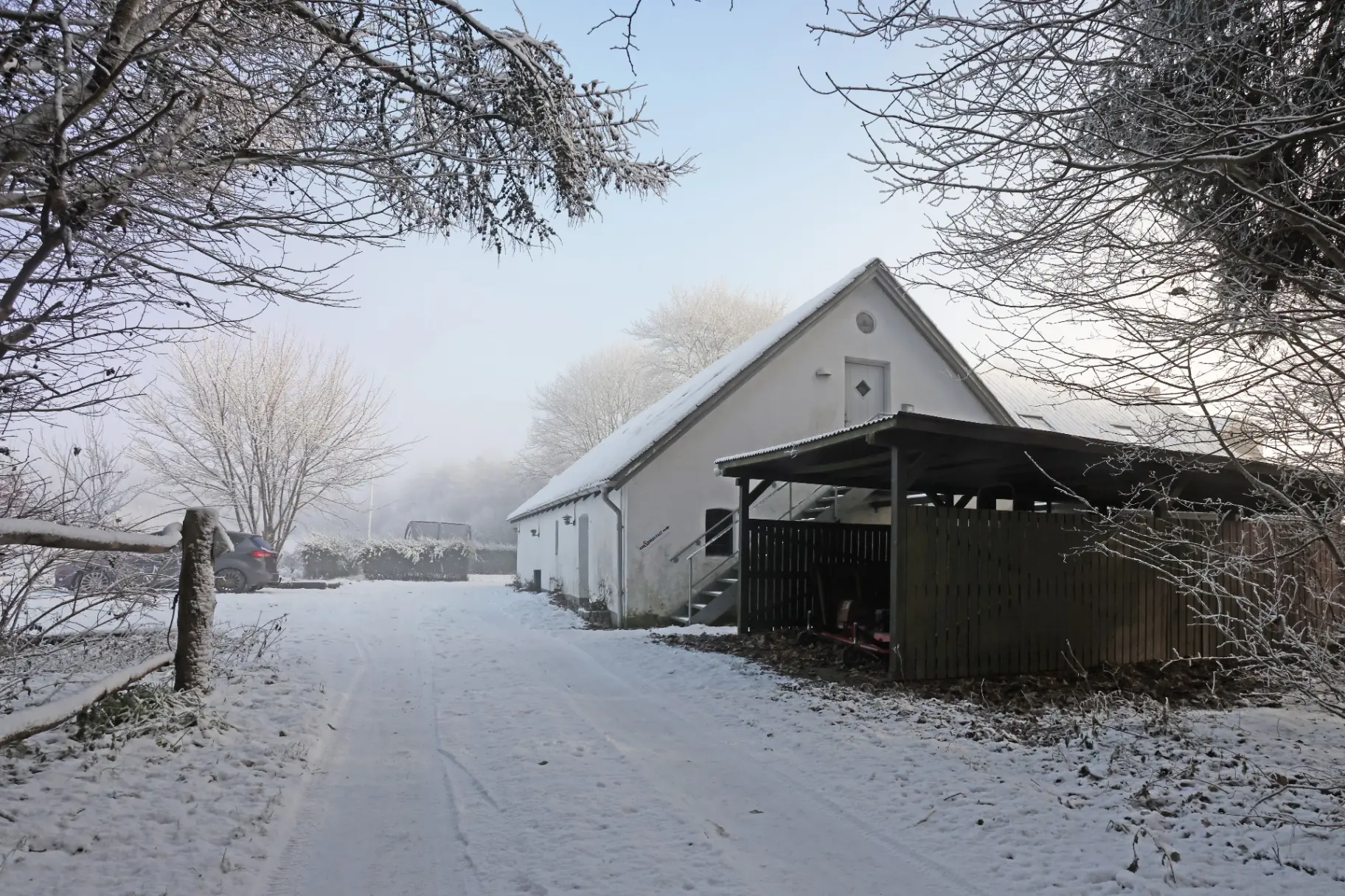 Snedækket gårdsplads foran den hvide længe, hvor en udvendig trappe fører op til døren