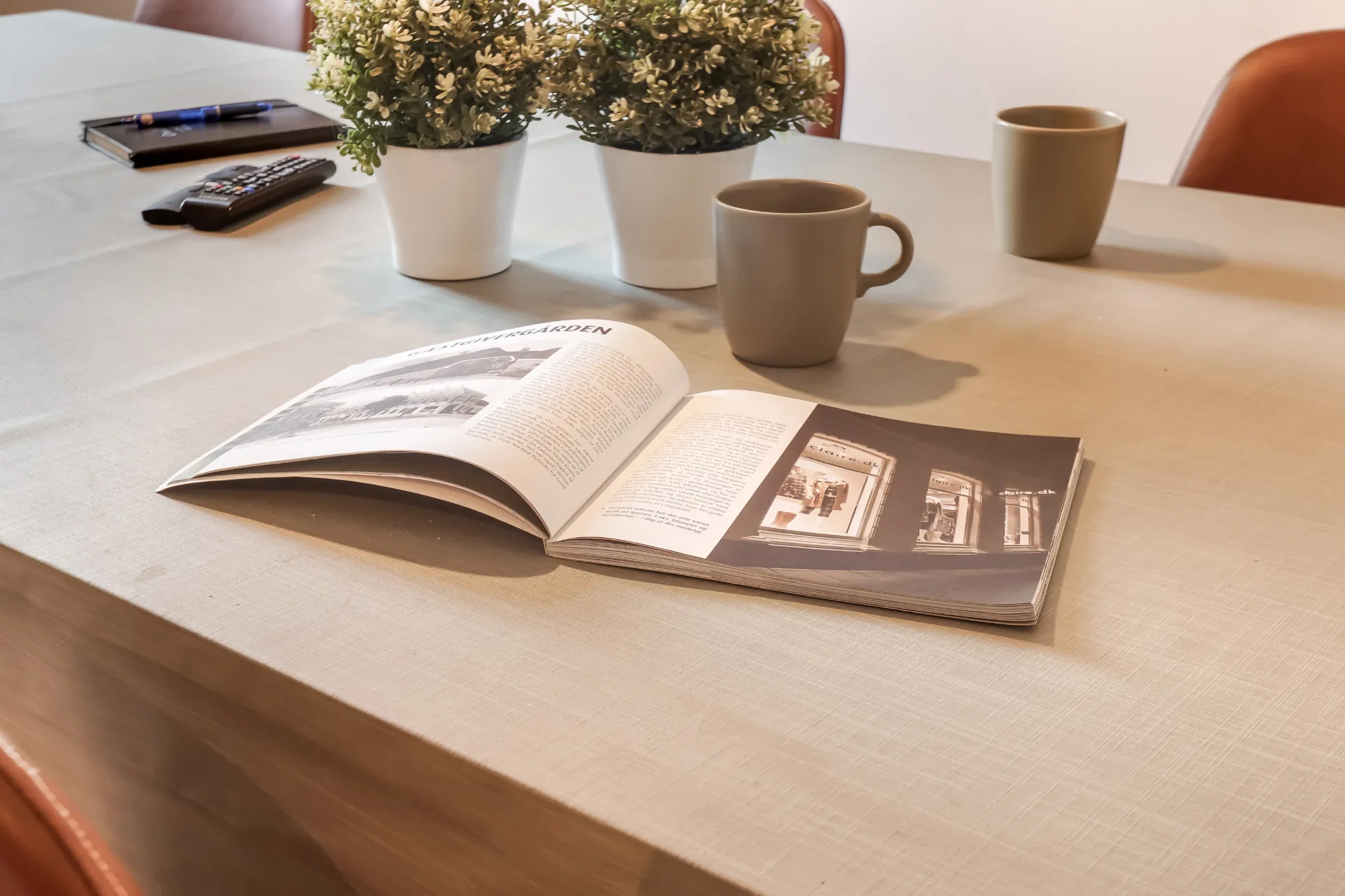 Opslået blad, to krus og en notesbog på det lange bord